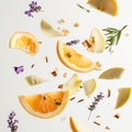 Eine künstlerische Darstellung der Duftnoten von Anfas Dhai mit Apfelscheiben, Zitronenzesten, Lavendelzweigen, Grapefruitsegmenten, Amberharz, Zedernholzspänen, Birnenscheiben, Geranienblüten, Vetiverwurzeln, Rosenblüten, Eichenmoos, Vanilleschoten, weißen Moschuselementen und Sandelholzstücken auf hellem Hintergrund